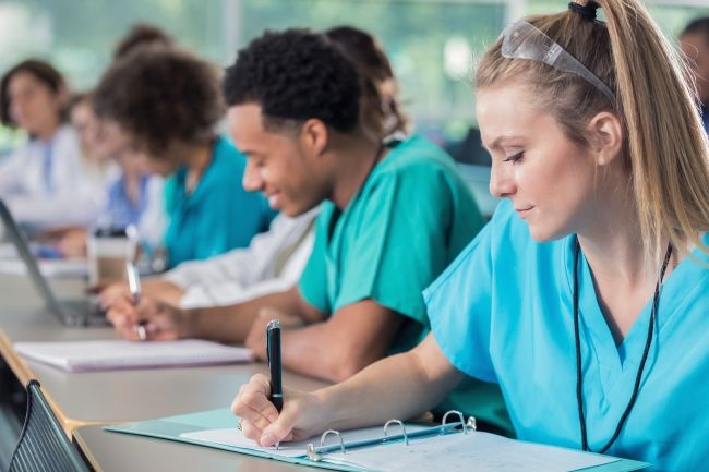 A group of nurses seated at a table, focused on writing notes and study