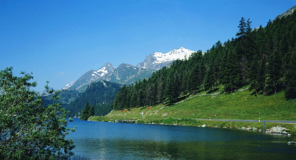 Blue sky view of a clear river, with snow-capped mountains in the distance.