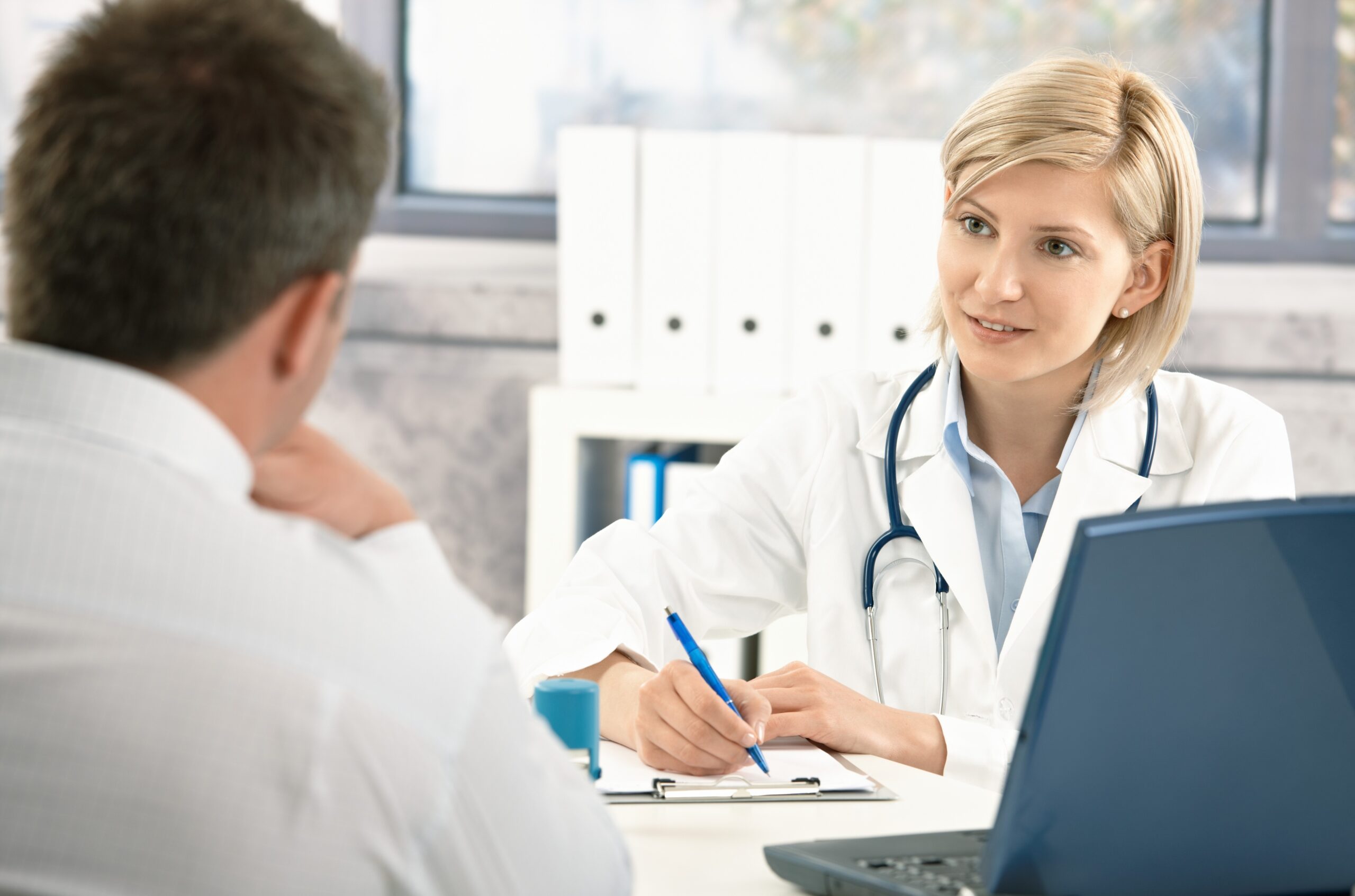 Seated female doctor taking notes with seated male patient