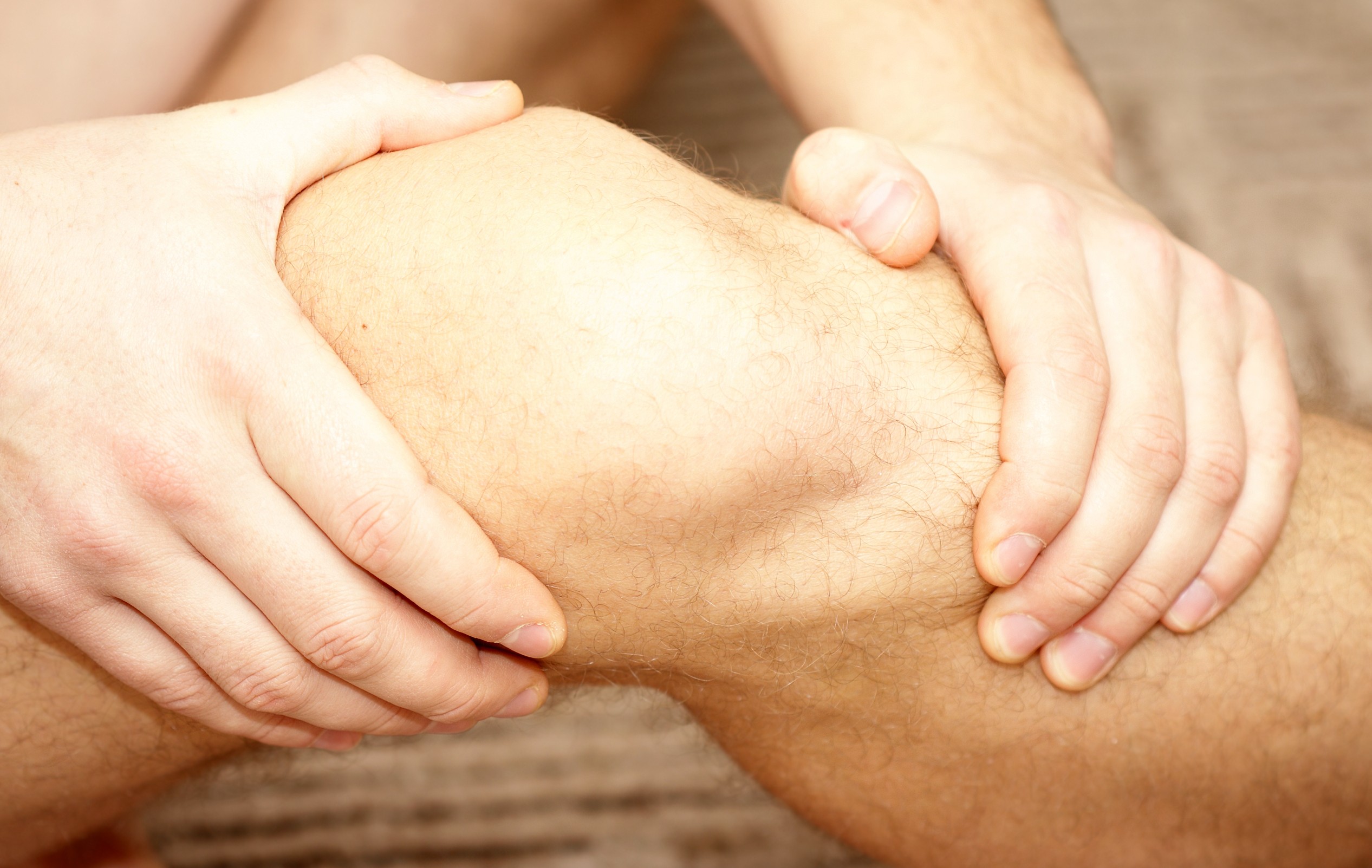 Closeup of hands grasping patient's knee pain