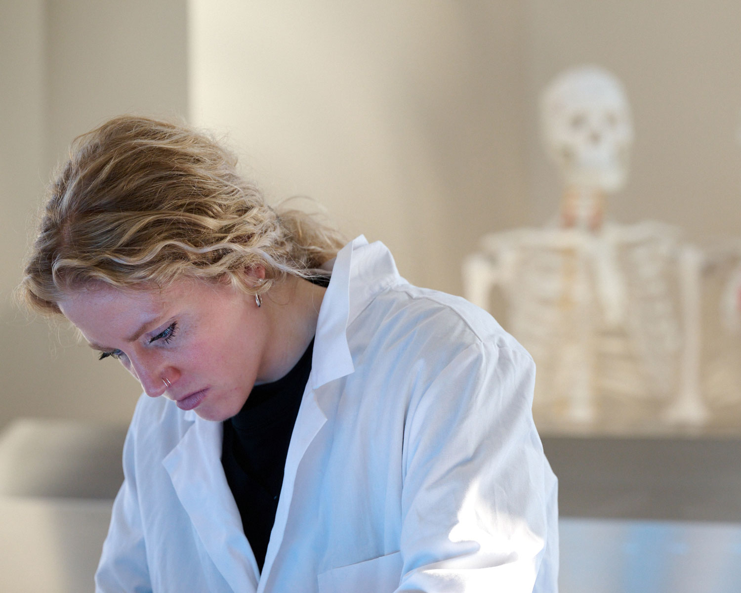 female student working in anatomy lab with skeleton model behind her
