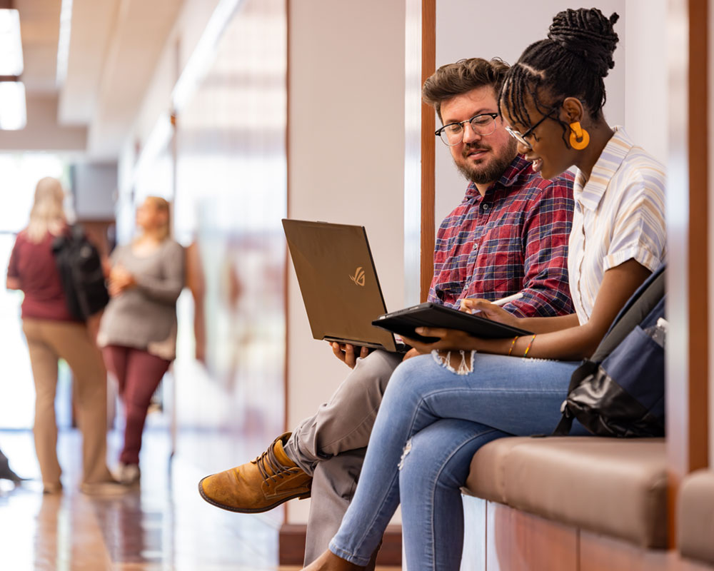 students sitting in janse hallway on laptop