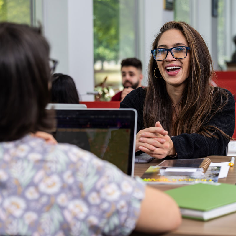 femal student smiling while studying with classmates in the library