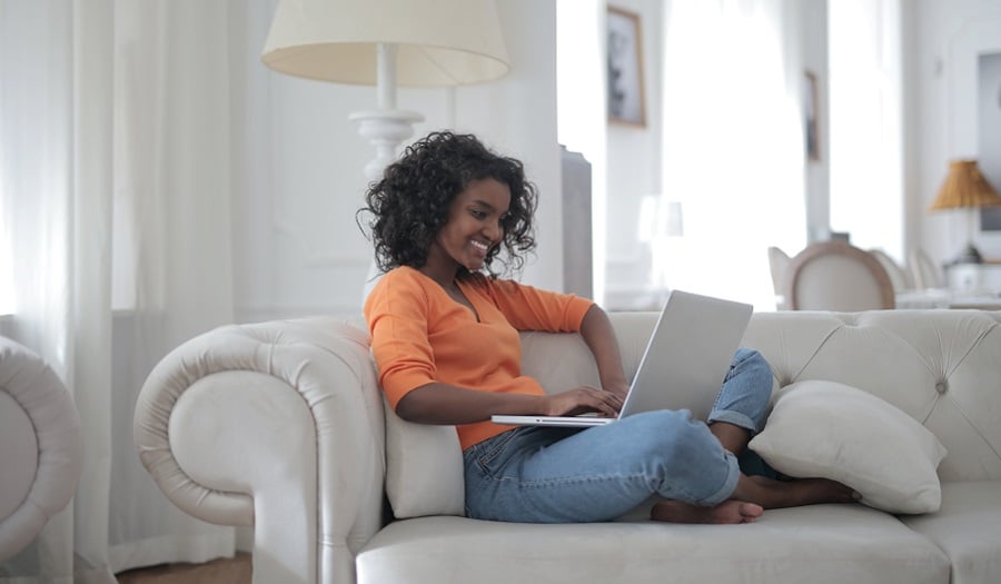 Woman sitting on white couch using laptop computer